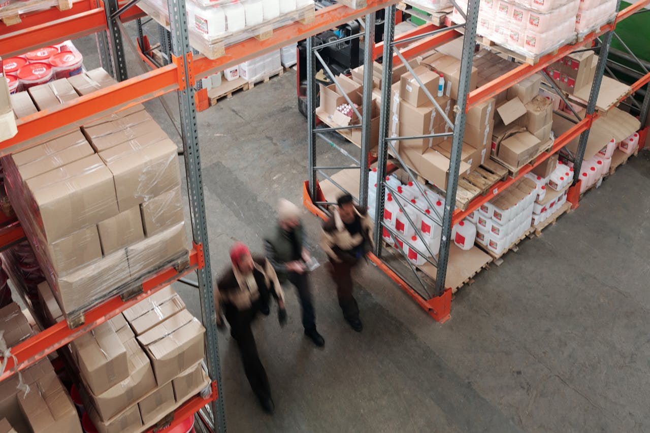trusted-partner A high angle view of workers in motion in a busy warehouse with shelves full of boxes and packages.