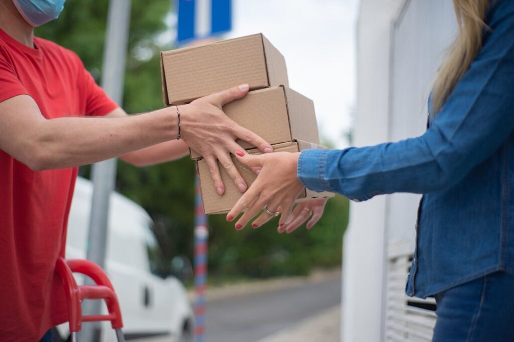 pexels photo 7844012 Hands exchanging cardboard boxes during an outdoor delivery scene.